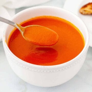 A spoonful of tomato soup being scooped from a large bowl of soup.