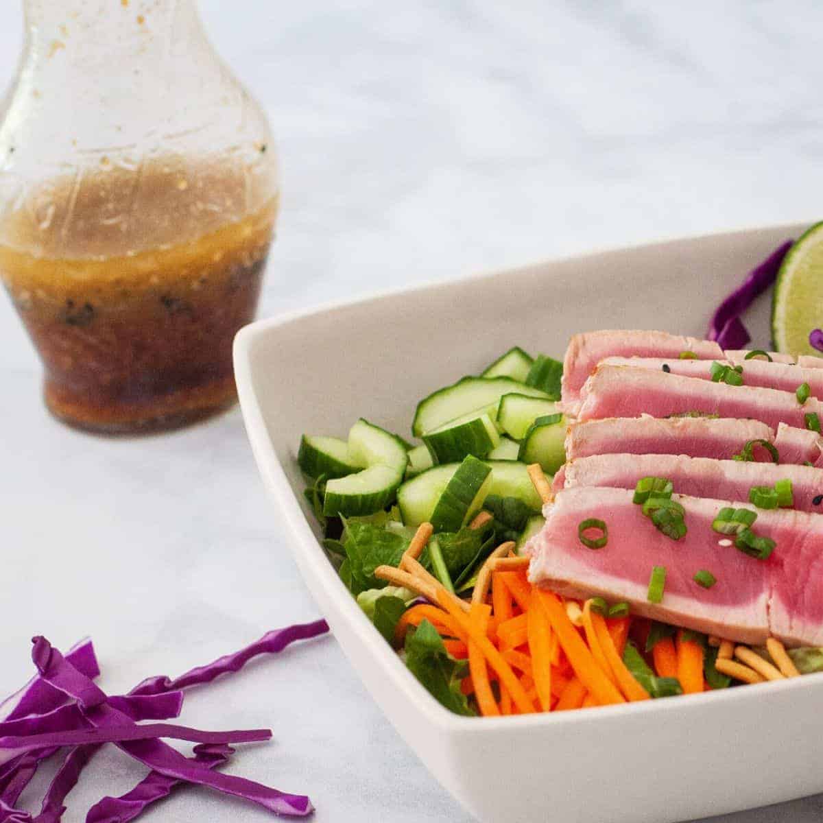 Soy ginger vinaigrette shown in a glass bottle set beside a large salad.