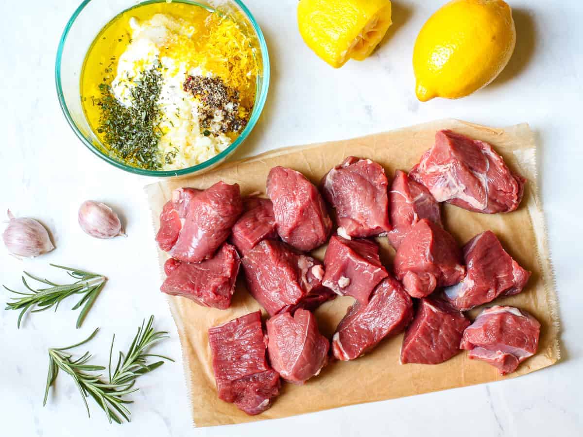 Chunks of lamb for the kebabs shown on a counter beside the Greek yogurt marinade mixture in a bowl. 