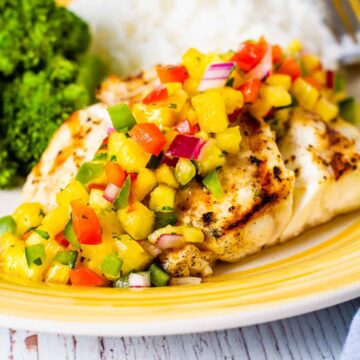 Grilled red snapper shown on a yellow dish topped with fresh pineapple salsa.