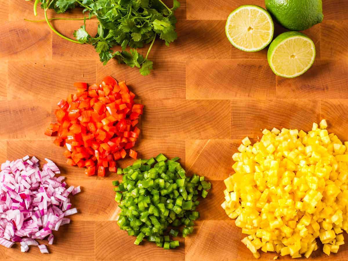 Ingredients for pineapple salsa shown in piles on a wooden cutting board.