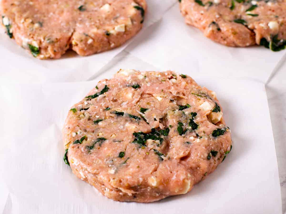 Raw turkey burger patties with spinach and feta.