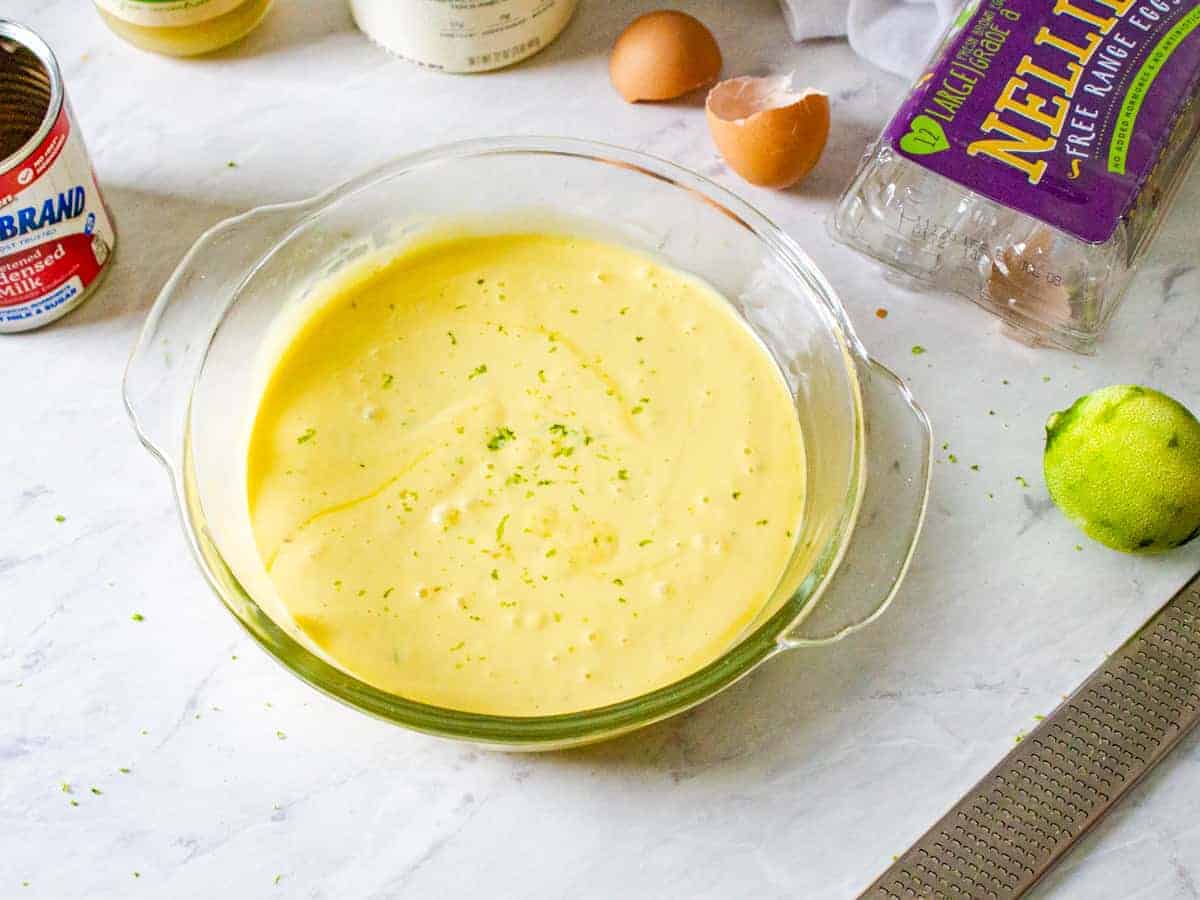 Key lime pie filling mixture shown in a glass mixing bowl surrounded by the ingredients.