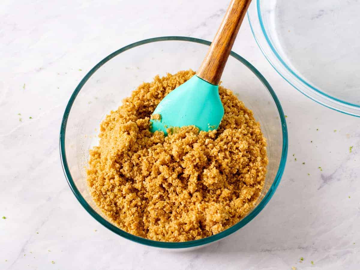 Mixture of graham cracker crumbs, brown sugar, and melted butter shown stirred together in a glass mixing bowl.