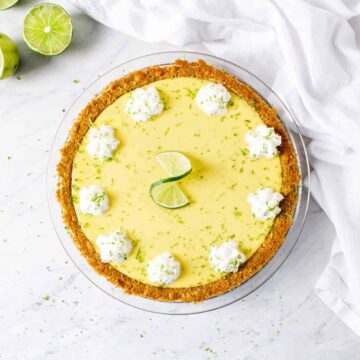 Overhead shot of whole key lime pie, topped with whipped cream, lime zest , and a lime twist.