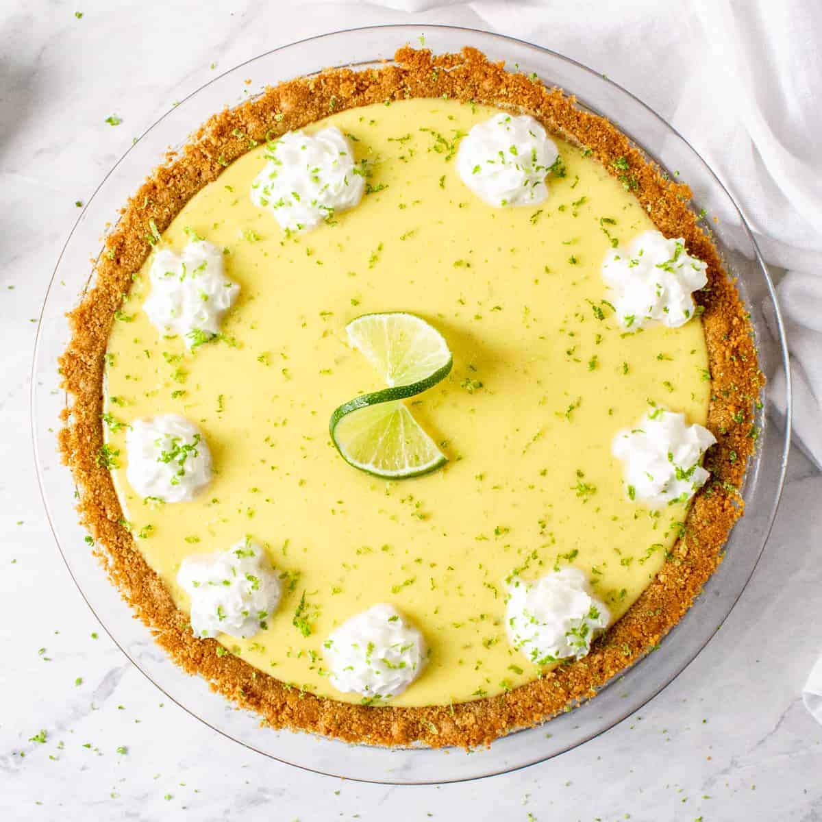 Close up overhead shot of finished key lime pie, topped with whipped cream, lime zest , and a lime twist.