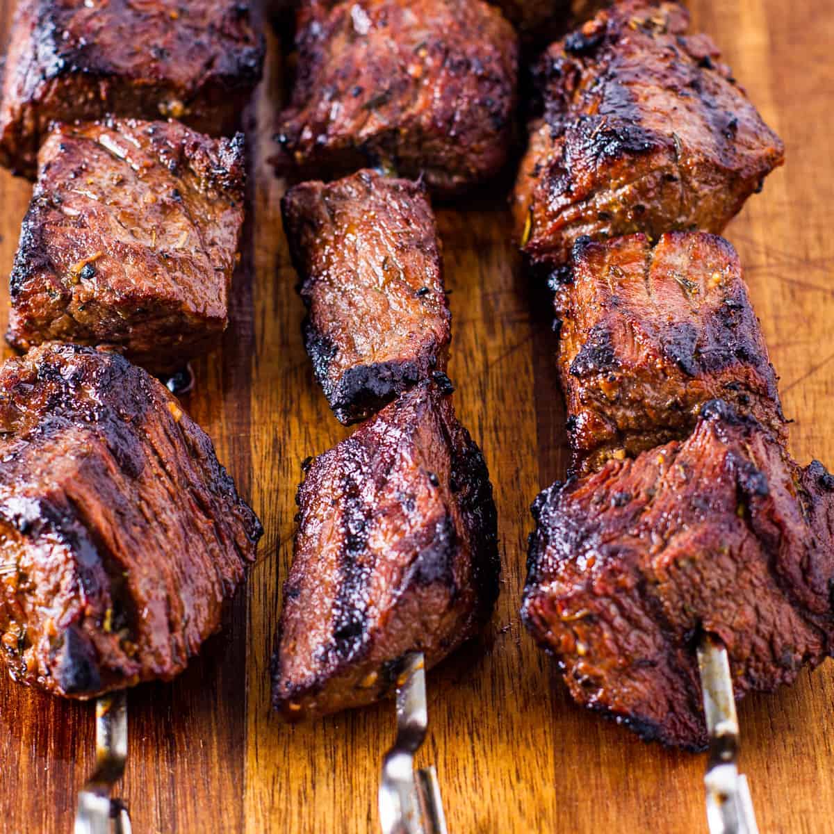 Finished steak kabobs resting on a wooden cutting board.