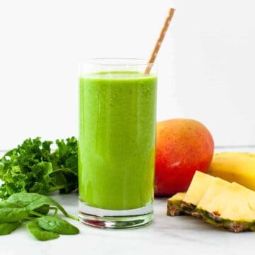 Tropical green smoothie in a glass, surrounded by fresh fruits and greens