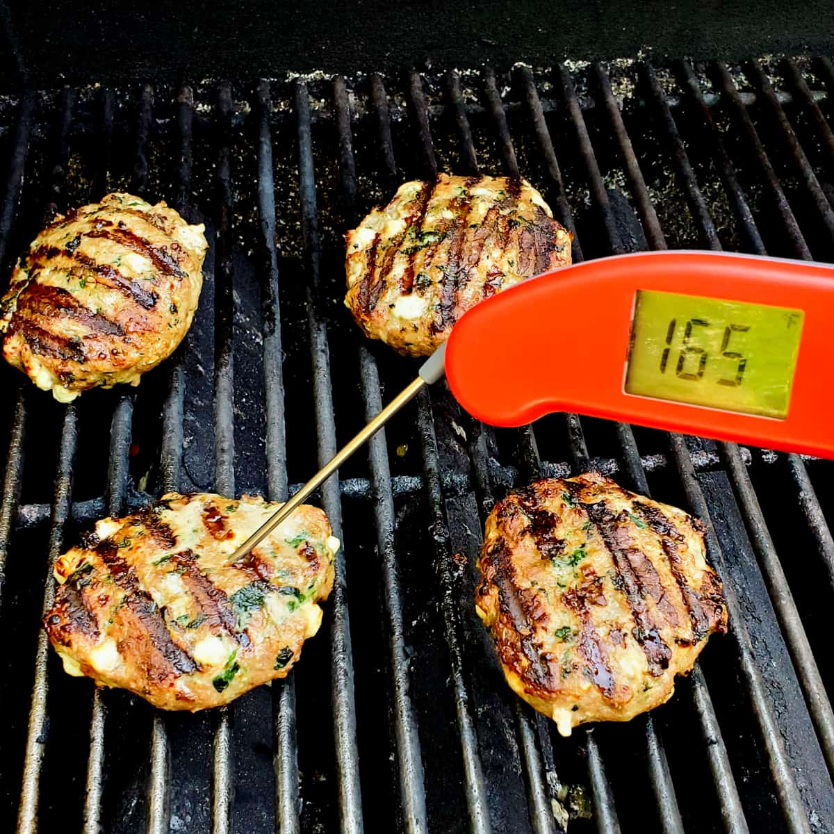 Cooked turkey burgers on the grill with a thermometer instered showing a final temperature of 165 degrees.