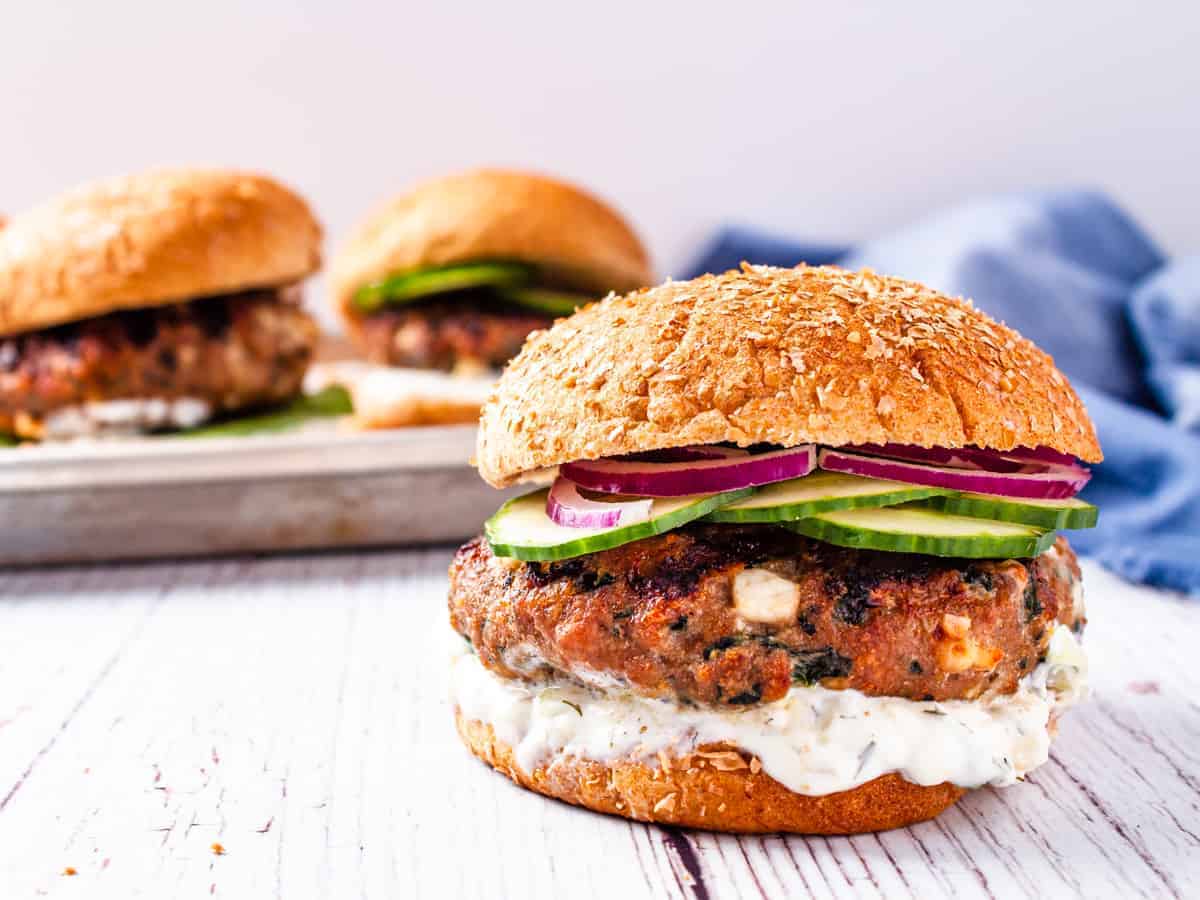 A single spinach and feta turkey burger in the foreground and a platter of burgers blurred in the background/