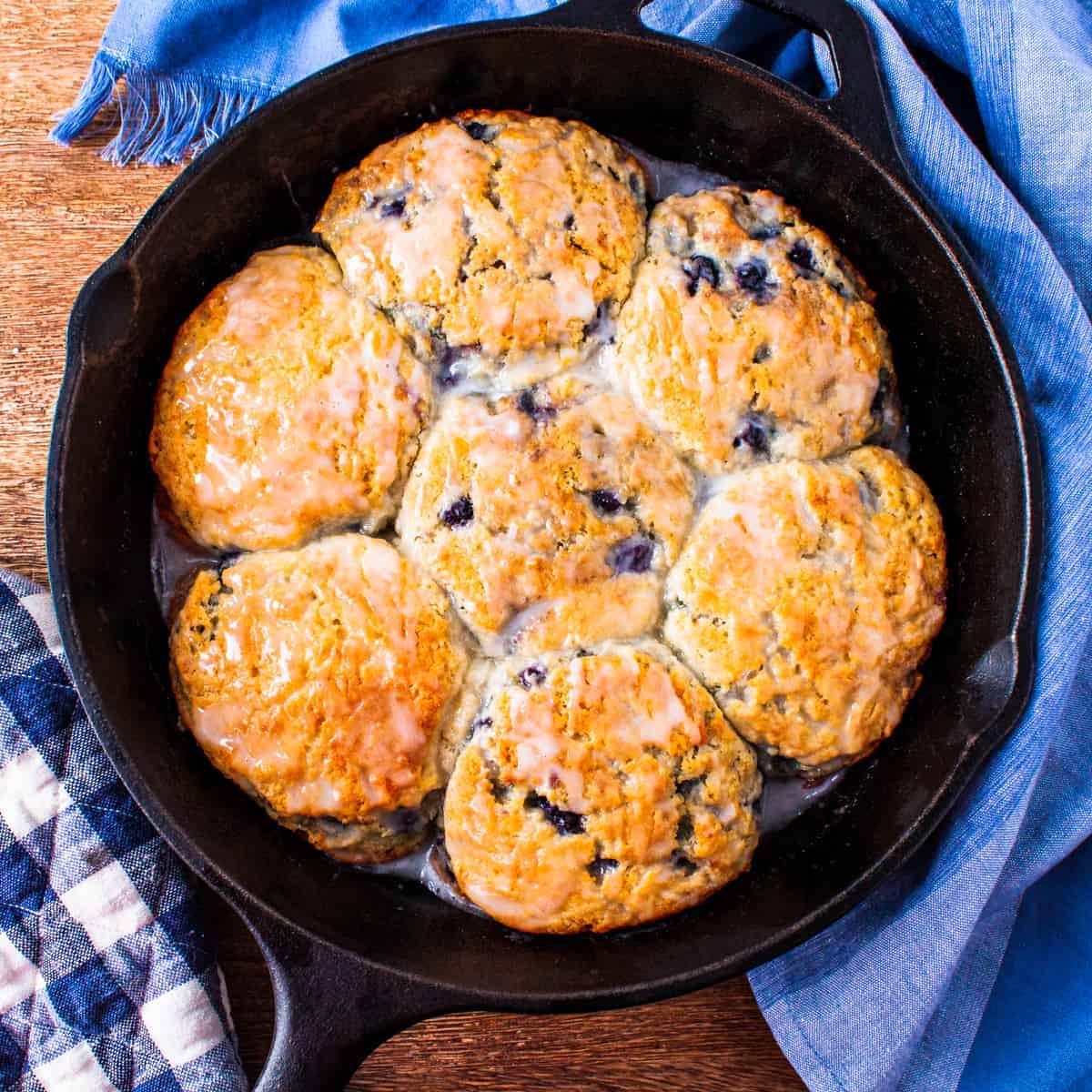 Overhead view of a cast iron skillet full of golden brown glazed blueberry biscuits.