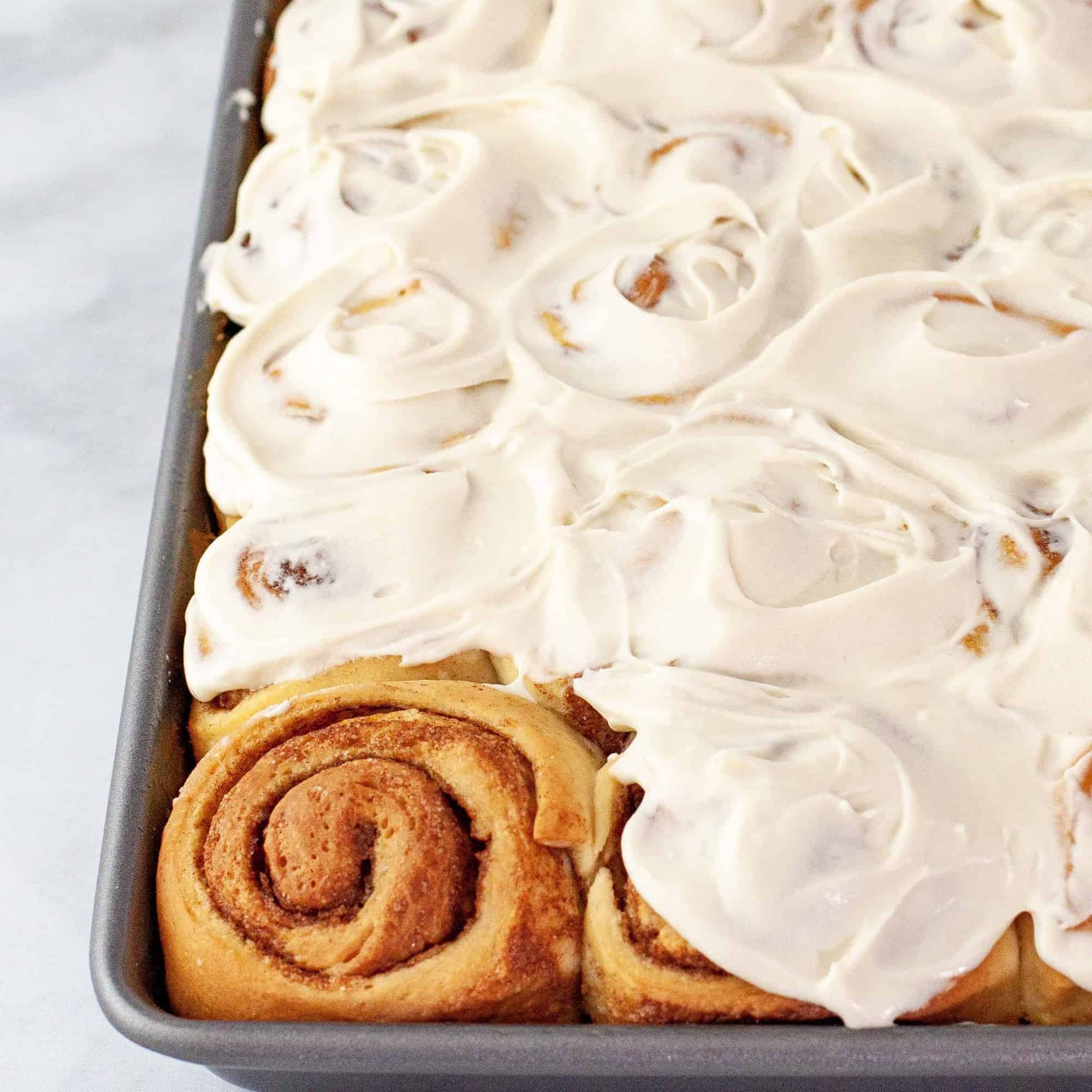 Overhead view of a pan of fresh baked cinnamon rolls with all but 1 roll iced.