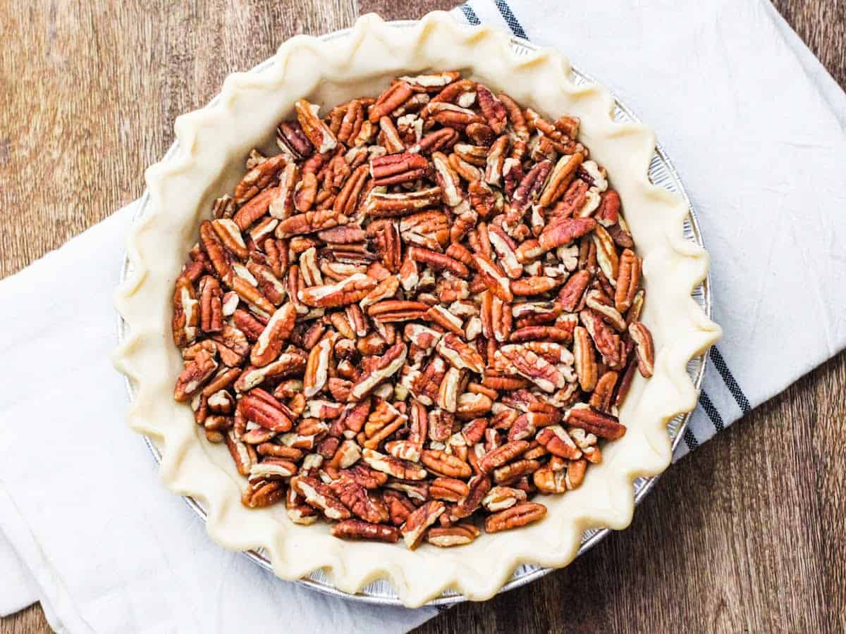 Overhead view of an unbaked pie crust filled with chopped pecans.