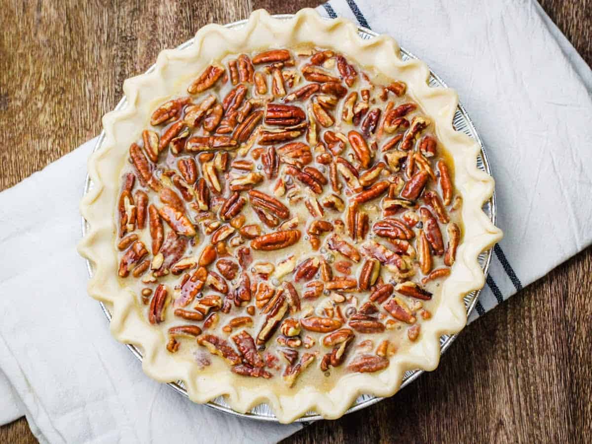 Overhead view of an unbaked pie crust filled with pecans and pecan pie filling ready to cook.