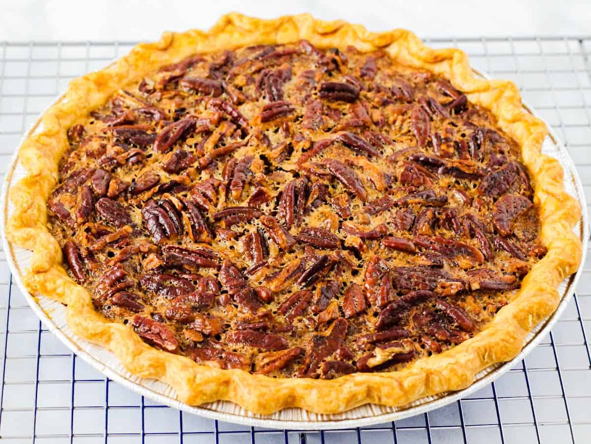 Side angle view of a baked pecan pie cooling on a wire rack.