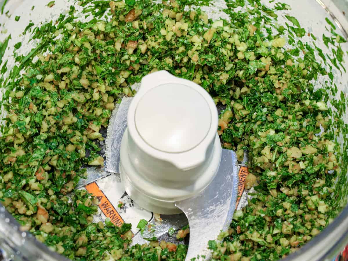 Close up image of pesto in a food processor after the initial blend to chop the ingredients and prior to adding the olive oil.