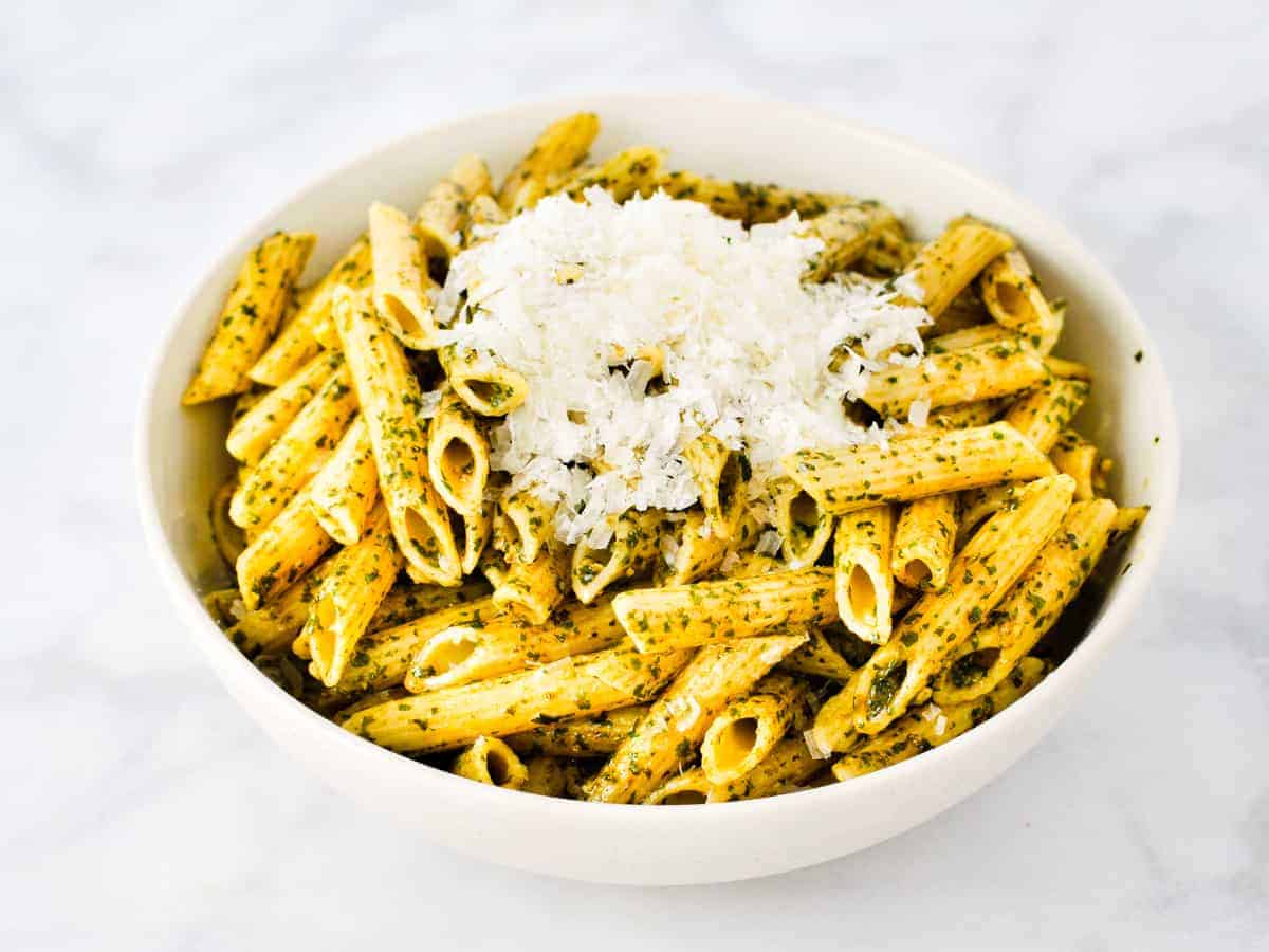 A large bowl of penne pasta tossed with pesto and topped with grated Parmesan cheese.