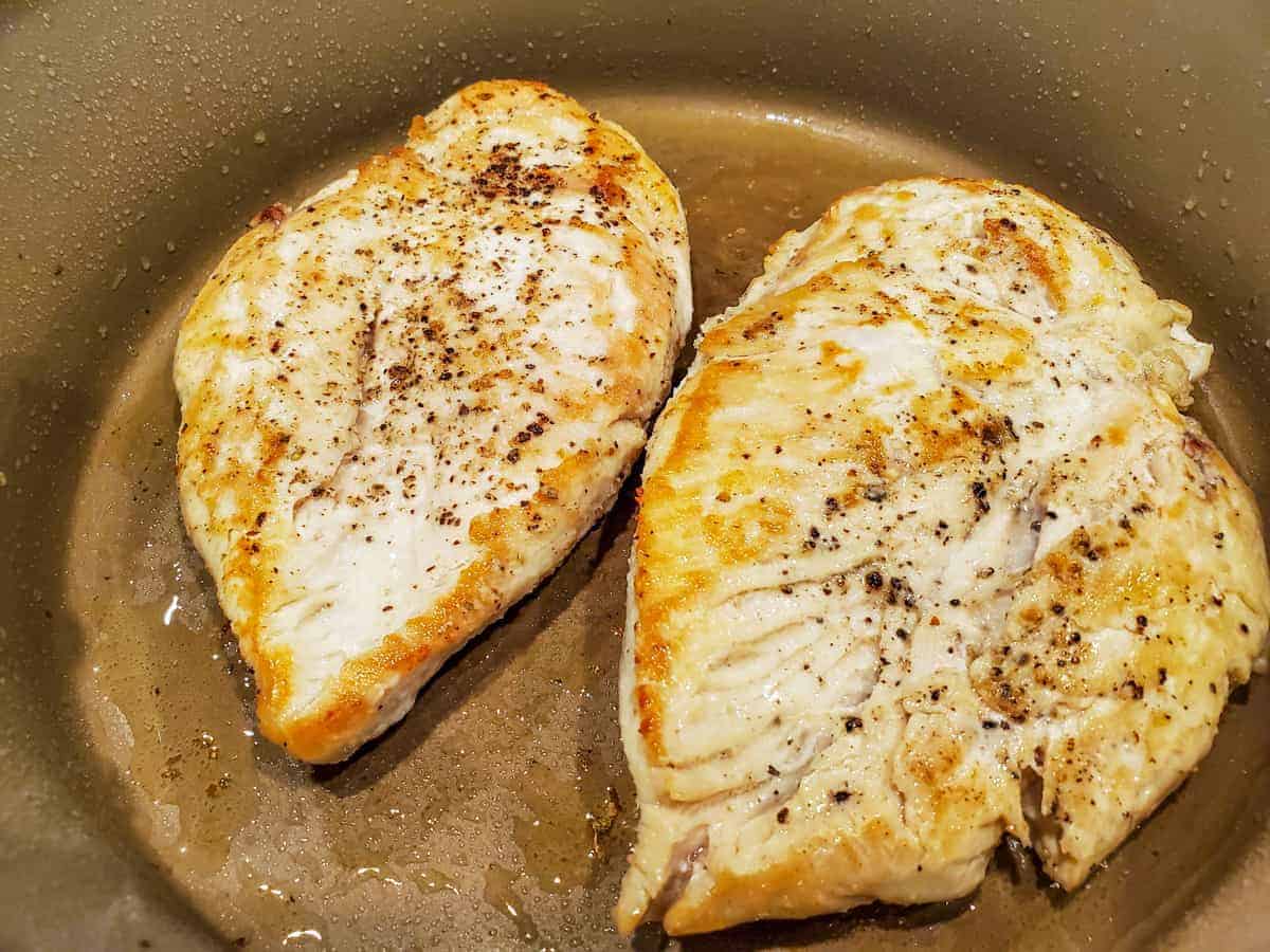 Chicken breasts being sautéed in a pan.