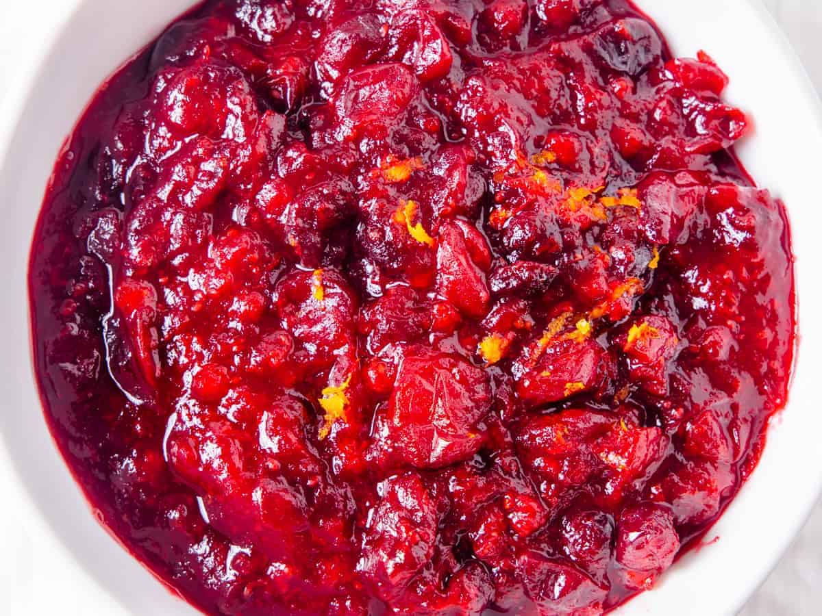 Overhead view of finished cranberry sauce served in a white bowl and topped with orange zest.