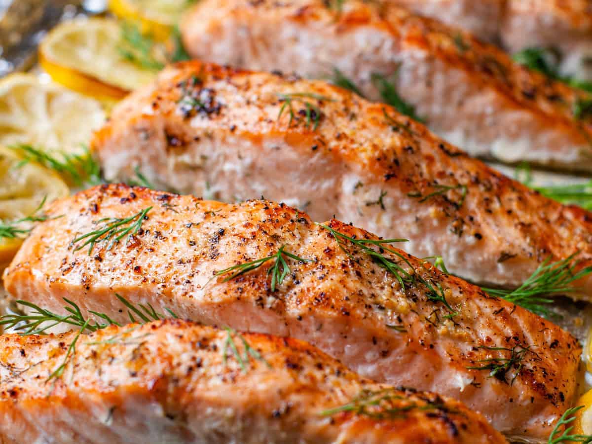 Side angle view of the sheet pan with salmon surrounded by lemon and fresh dill.