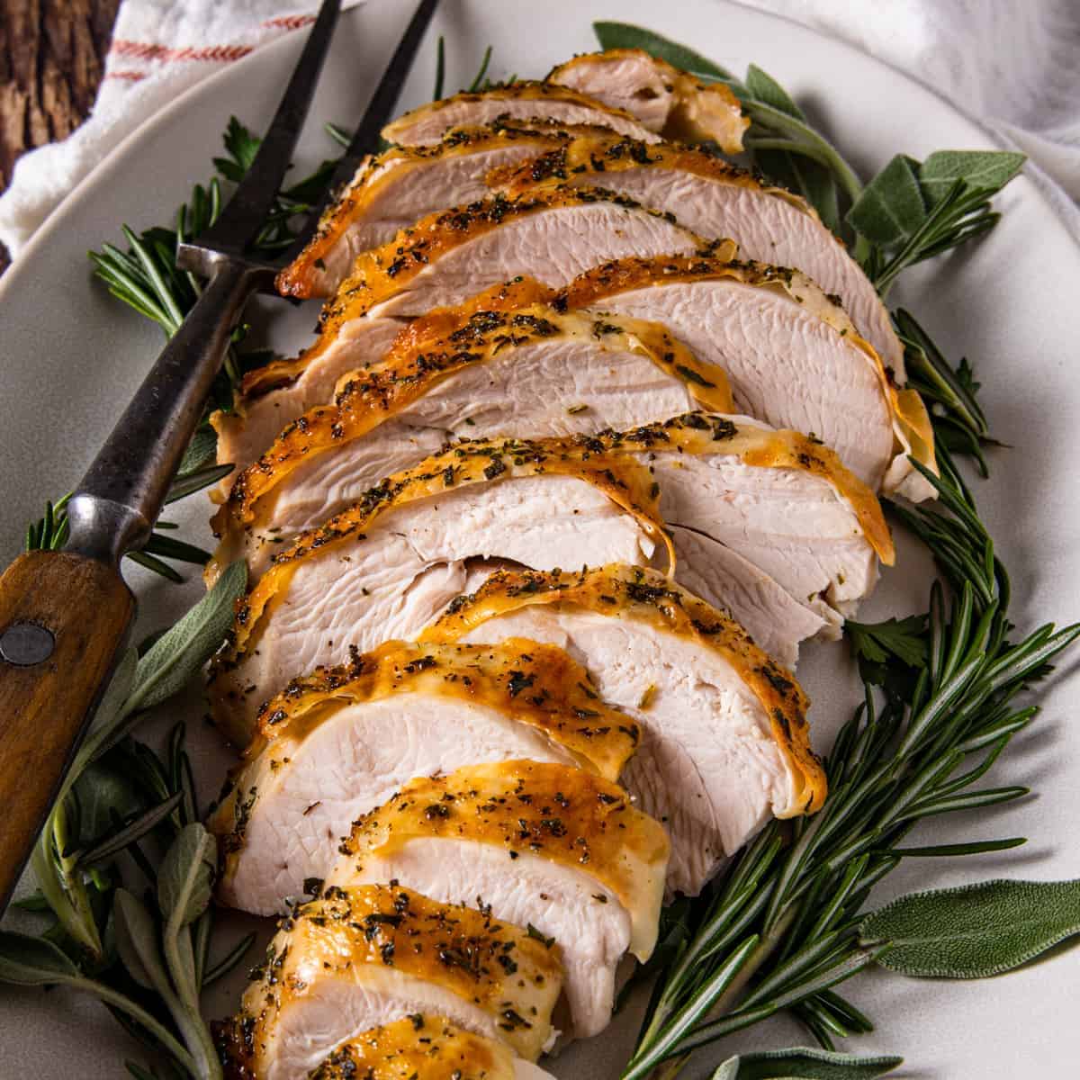 Close up view of the sliced herb roasted turkey on a serving platter surrounded by fresh herbs for garnish.