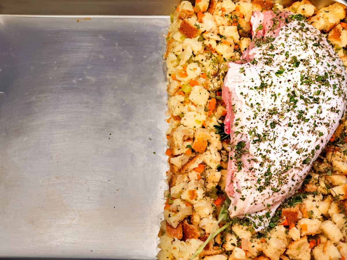 The seasoned turkey breast is shown set on top of the stuffing on about one third of the sheet pan. Leaving the rest of the pan open for the remaining vegetables.