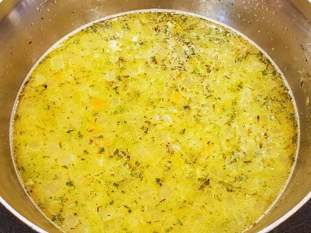 The chicken stock and seasonings are added to the pot with the vegetables and stirred to combine.