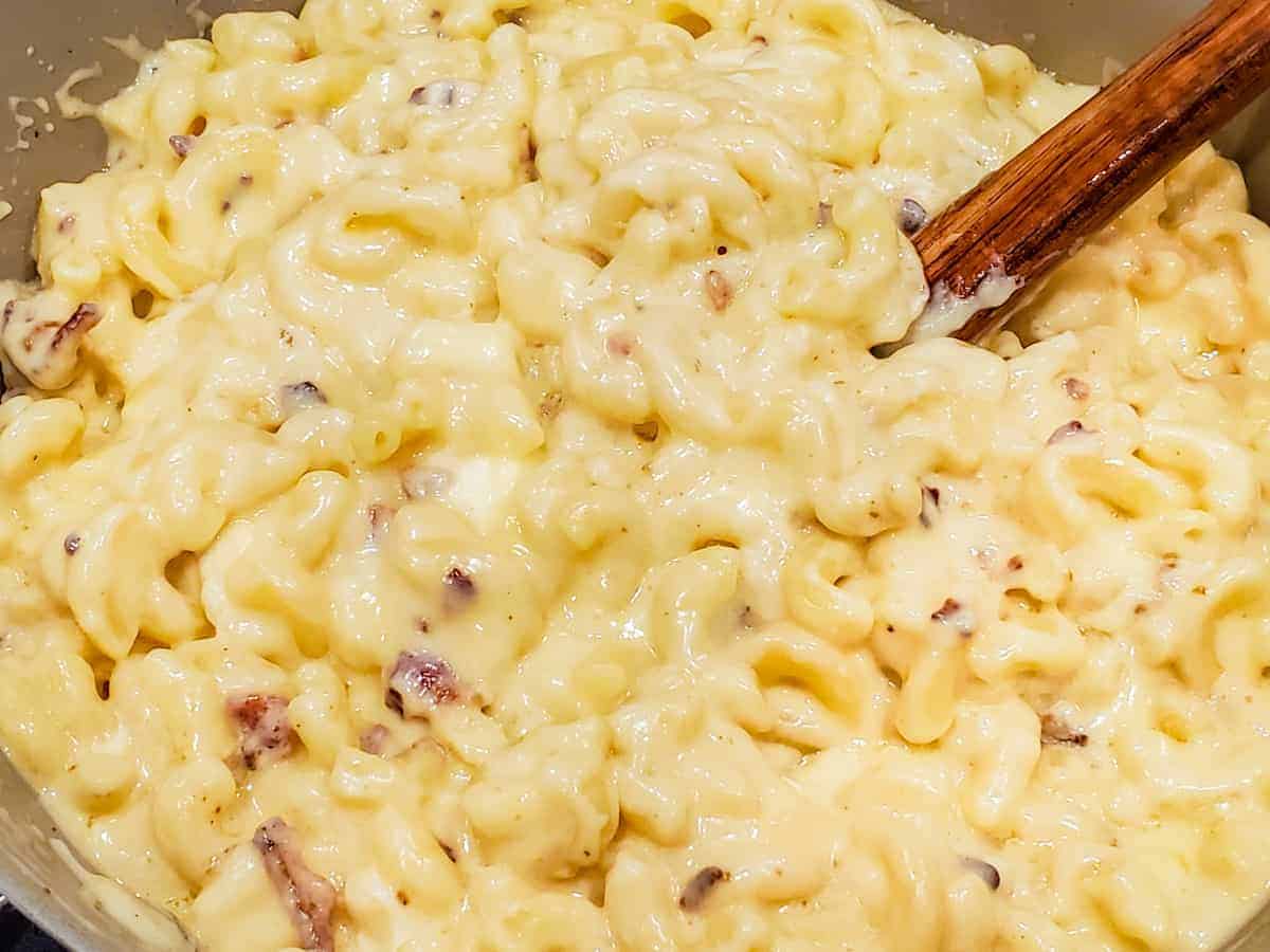 The cooked macaroni and bacon are added to the pot and stirred in with the cheese sauce.