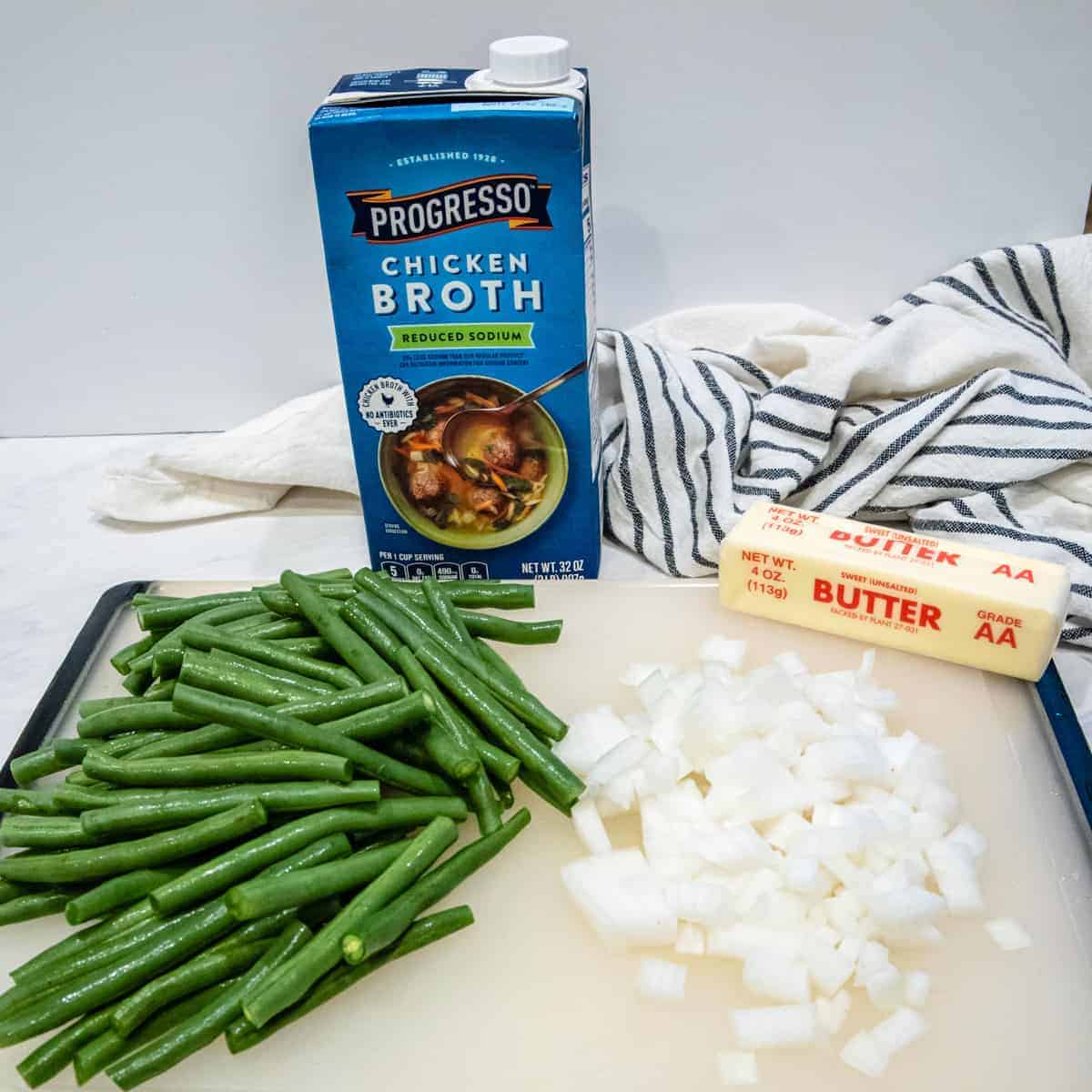 This image shows the ingredients needed for the dish. Fresh cut green beans shown alongside diced onion, chicken broth, and butter.