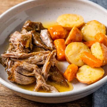 Instant pot pork roast served on a dish with potatoes and carrots.