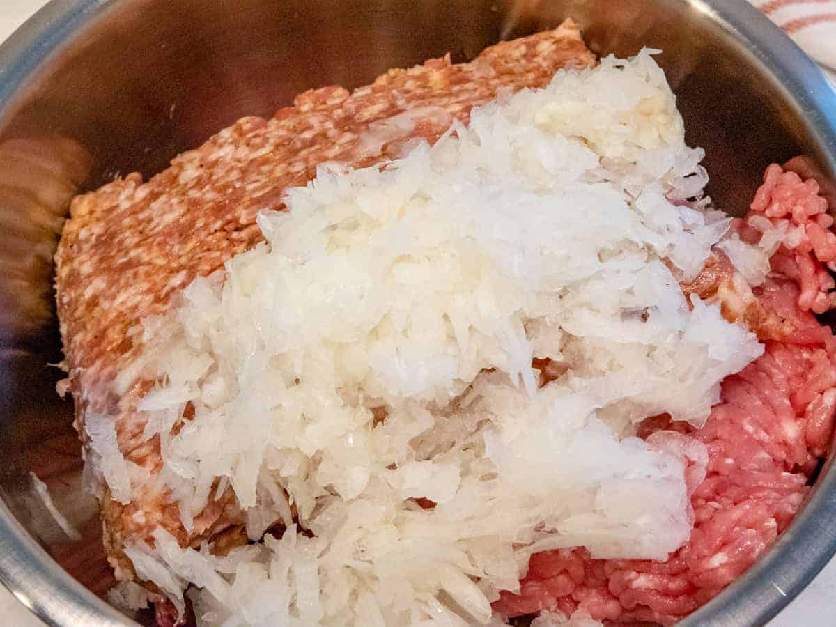 Onion, garlic and meat for meatballs in a mixing bowl. 