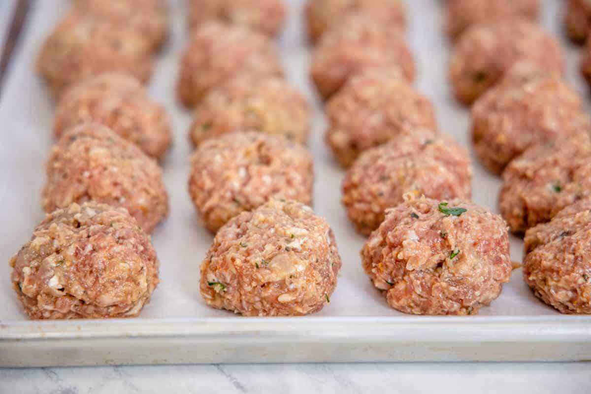 Raw meatballs shown set on a parchment lined baking sheet.