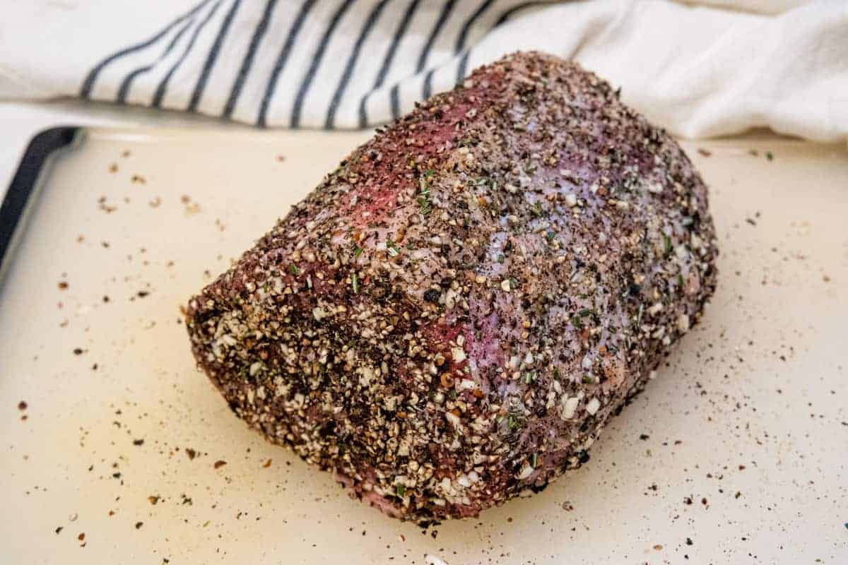 The eye round of beef is shown on a cutting board after applying the pepper seasoning rub.