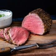 Roast beef shown sliced on a cutting board served with horseradish cream sauce.