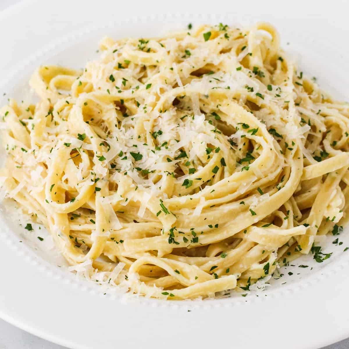 A large plate of fettuccine alfredo shown topped with freshly grated Parmesan cheese and chopped parsley.