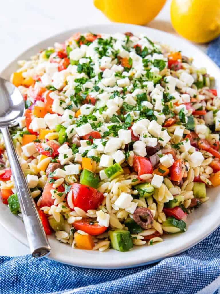 Side angle view of a serving platter piled high with Greek orzo pasta salad.