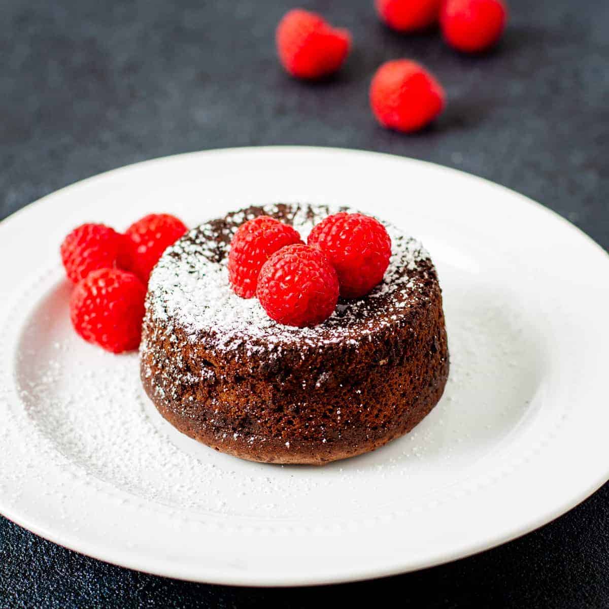 Lava cake served on a dish and topped with raspberries and powdered sugar.