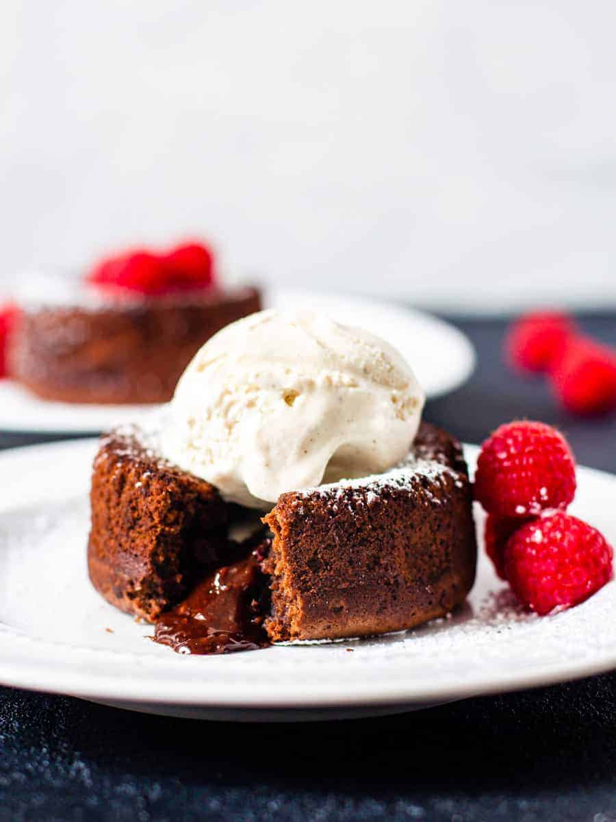 Close up of a chocolate molten lava cake topped with ice cream and cut open to reveal an oozy chocolate center.