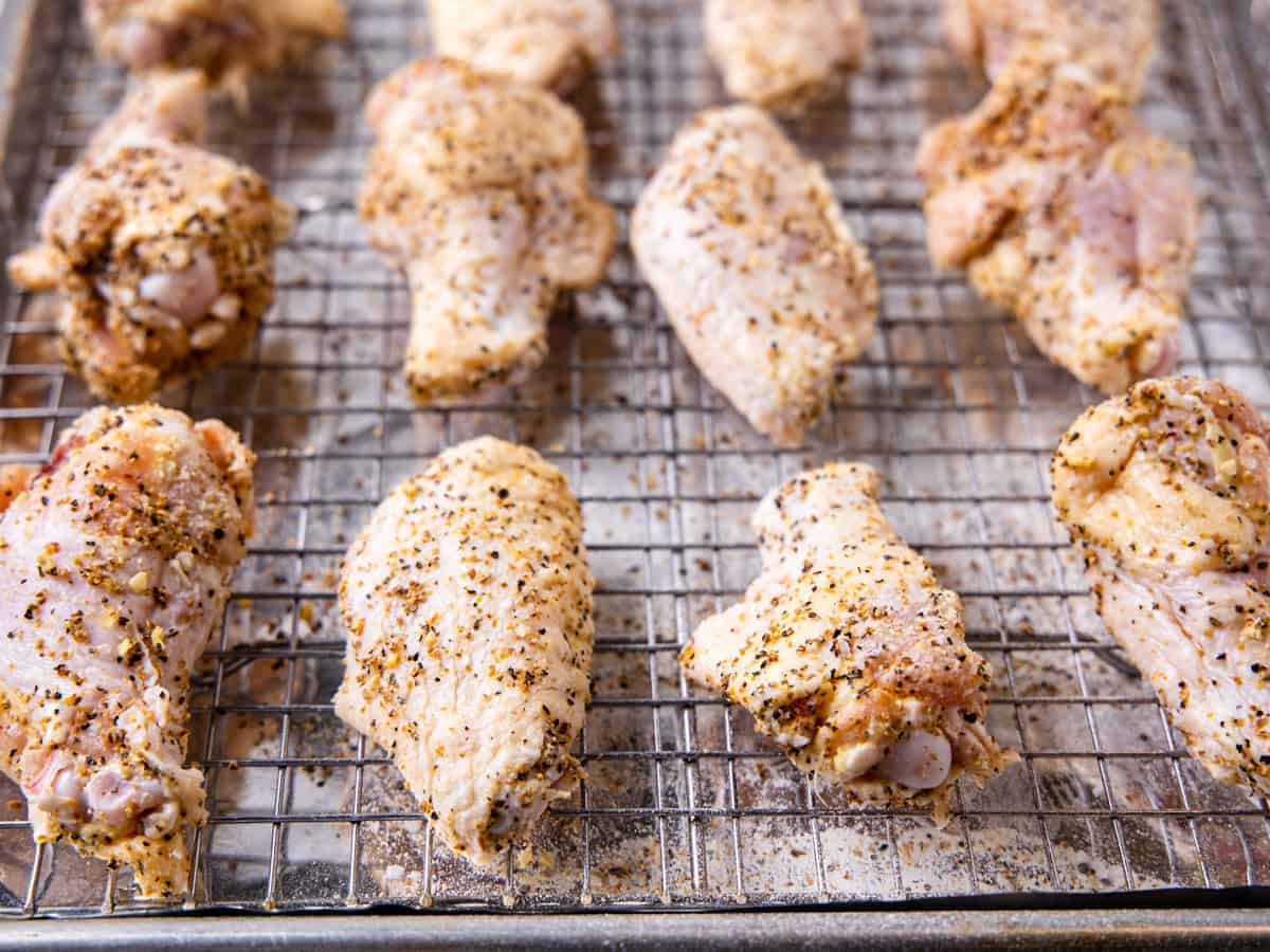 Chicken wings coated in lemon pepper seasoning and baking powder are shown set on a wire baking rack prior to cooking.