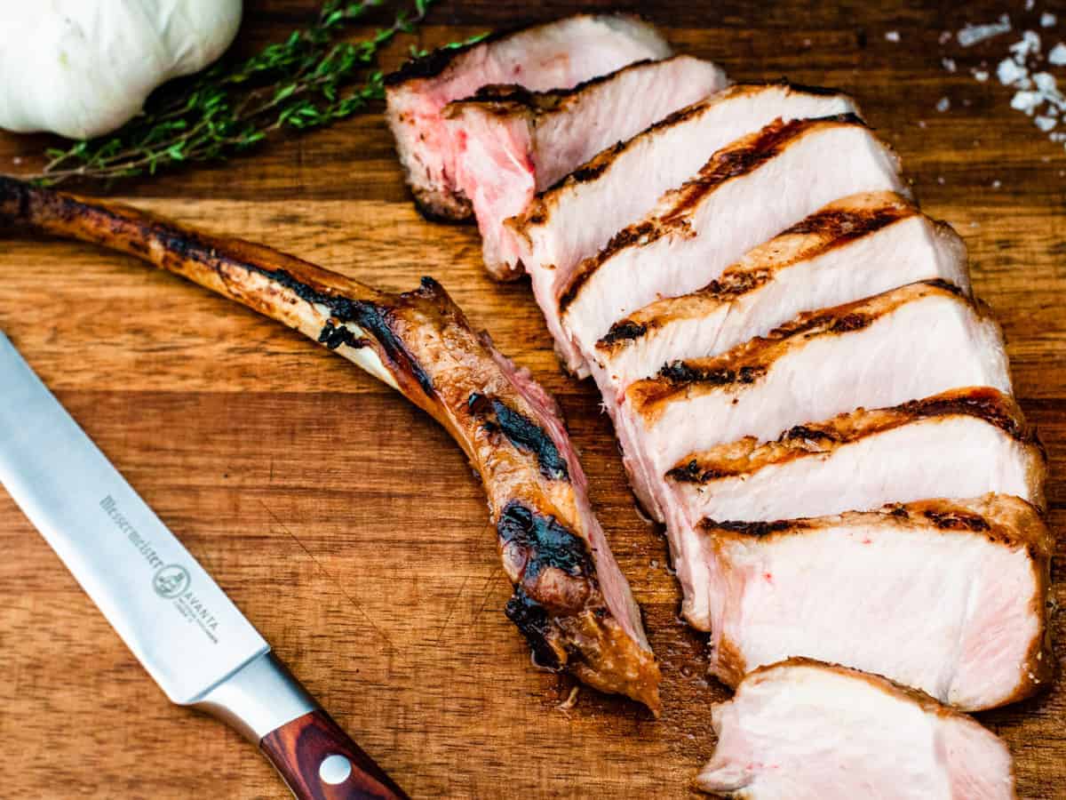 A grilled pork chop shown sliced on a cutting board.