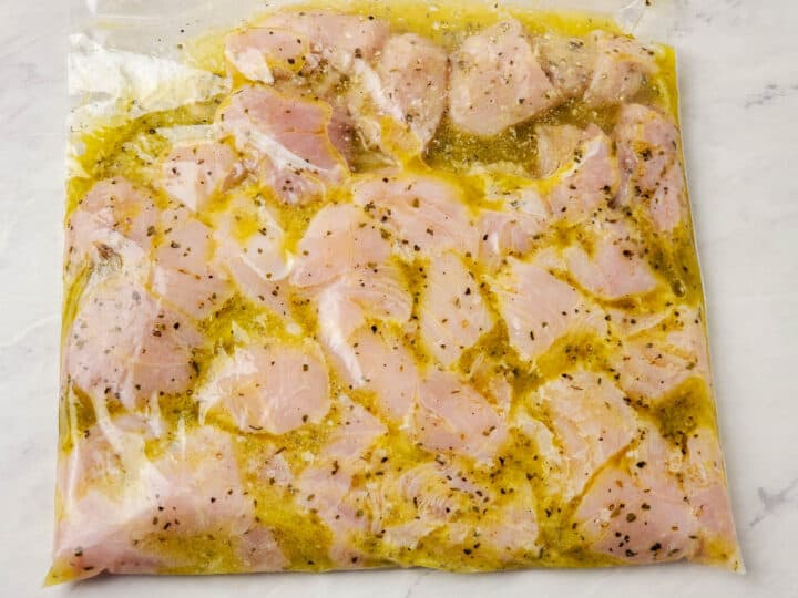 Chicken cubes shown marinating in a plastic bag.