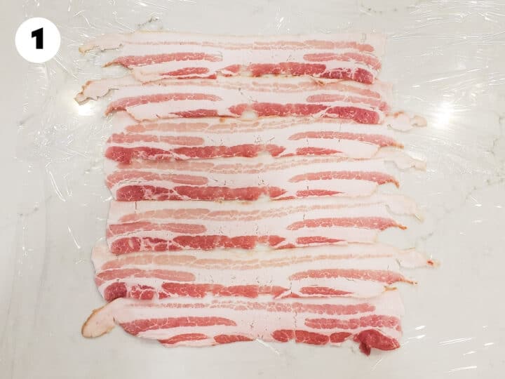 Slices of bacon laid in parallel rows, set on plastic wrap.