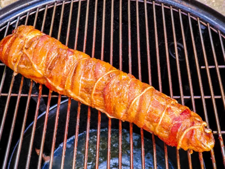 Bacon wrapped pork tenderloin shown on a smoker after cooking.