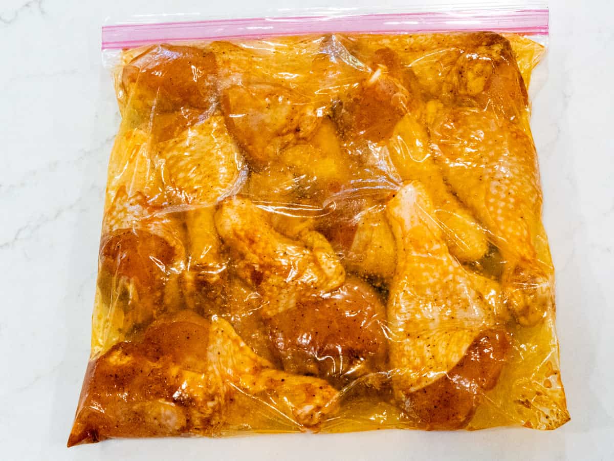 Chicken legs marinating in a plastic bag.
