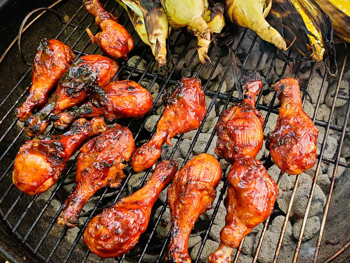 Chicken legs coaed with barbecue sauce being cooked on a grill.