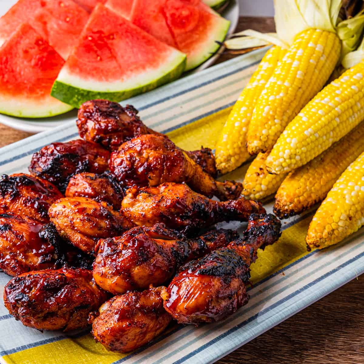 A platter of grilled chicken legs with corn and watermelon.
