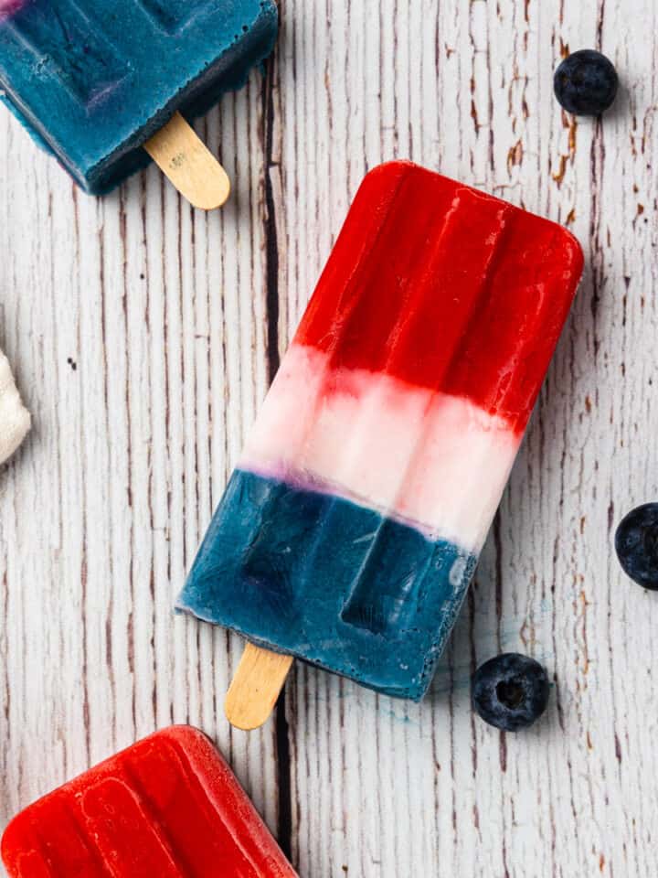 Red, white, and blue popsicles on a weathered white washed wood background.