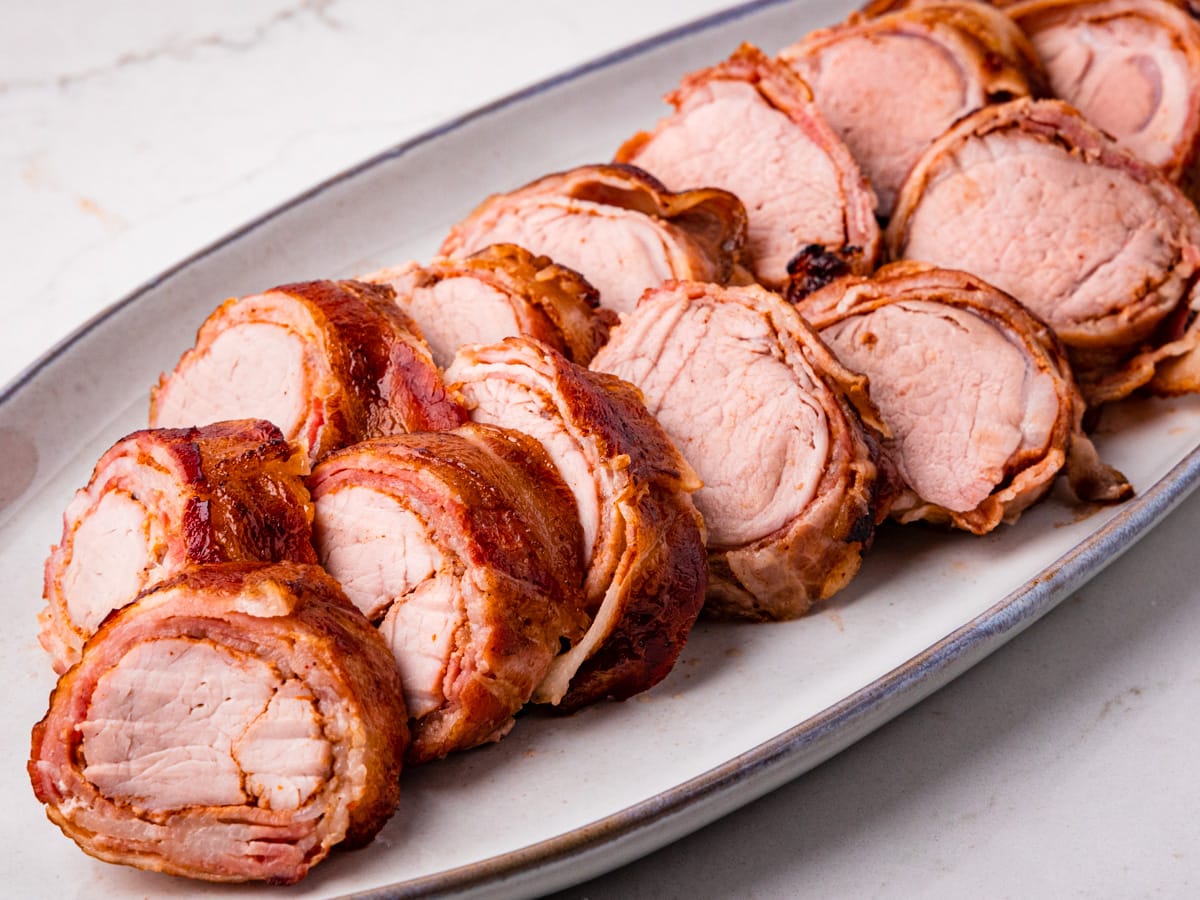 Slices of smoked pork tenderloin wrapped in bacon, served on a platter.