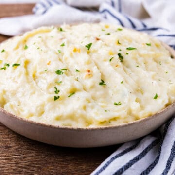A large bowl of roasted garlic mashed potatoes set on a wooden table.