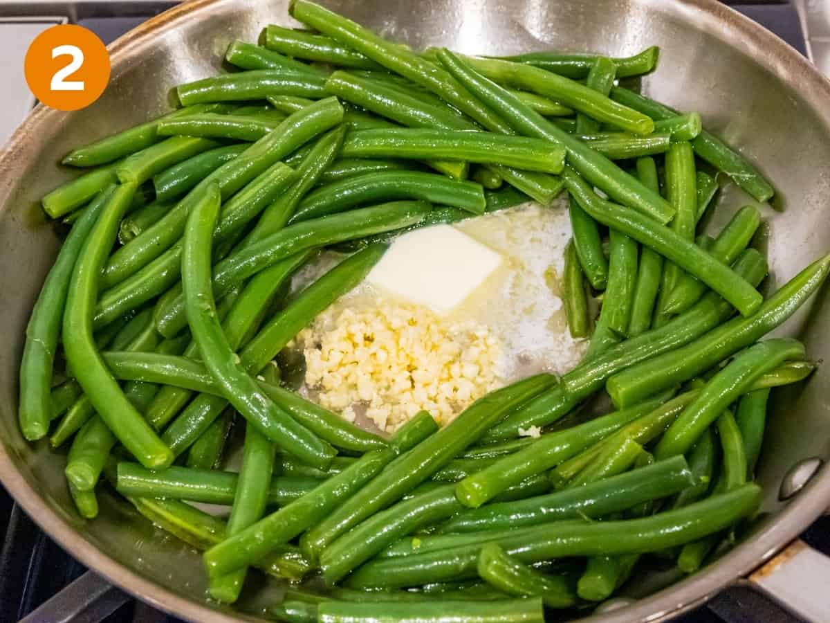 Garlic and utter cooking with green beans in a saute pan..